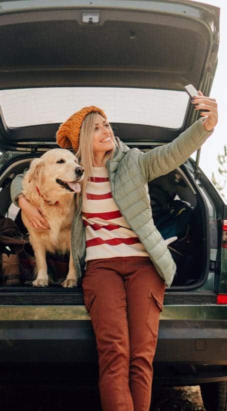 woman taking a selfie with a golden retriever on a road trip
