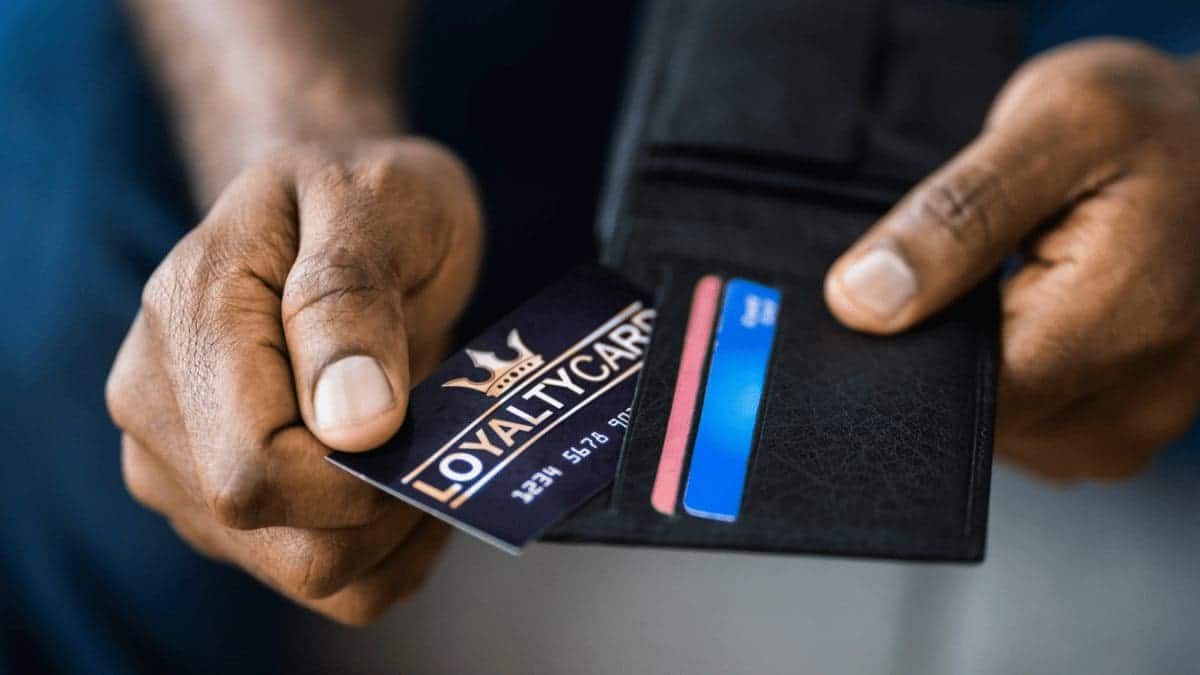A man sorting through multiple loyalty rewards cards in a black wallet. 
