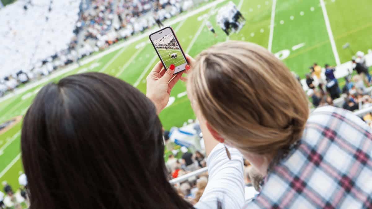 Two friends taking a picture at a sporting event available through unique offerings in travel rewards programs. 