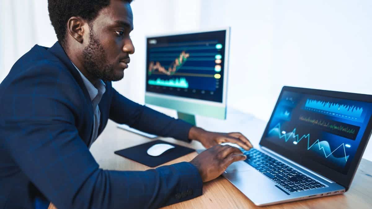 A man working with a laptop and computer screen analyzing blockchain in loyalty programs.
