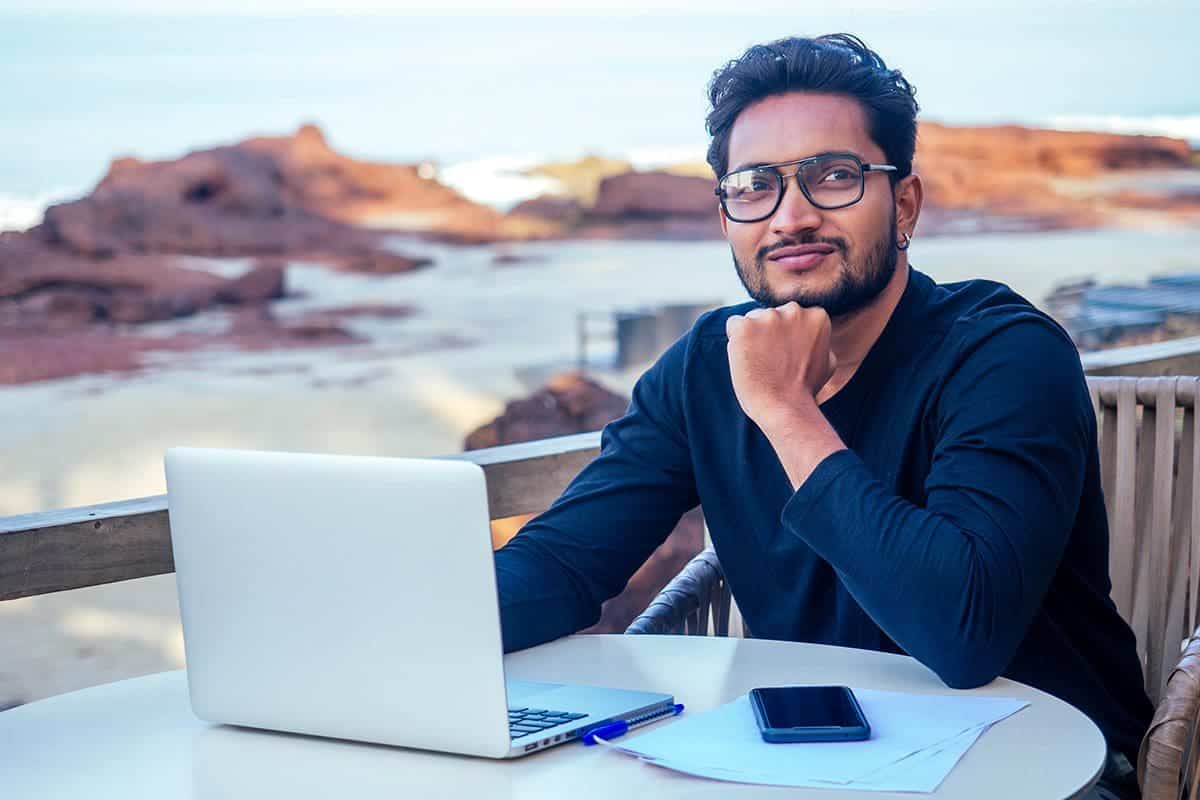 A man with a laptop on the beach by the ocean booked with points by an earn and burn loyalty program.