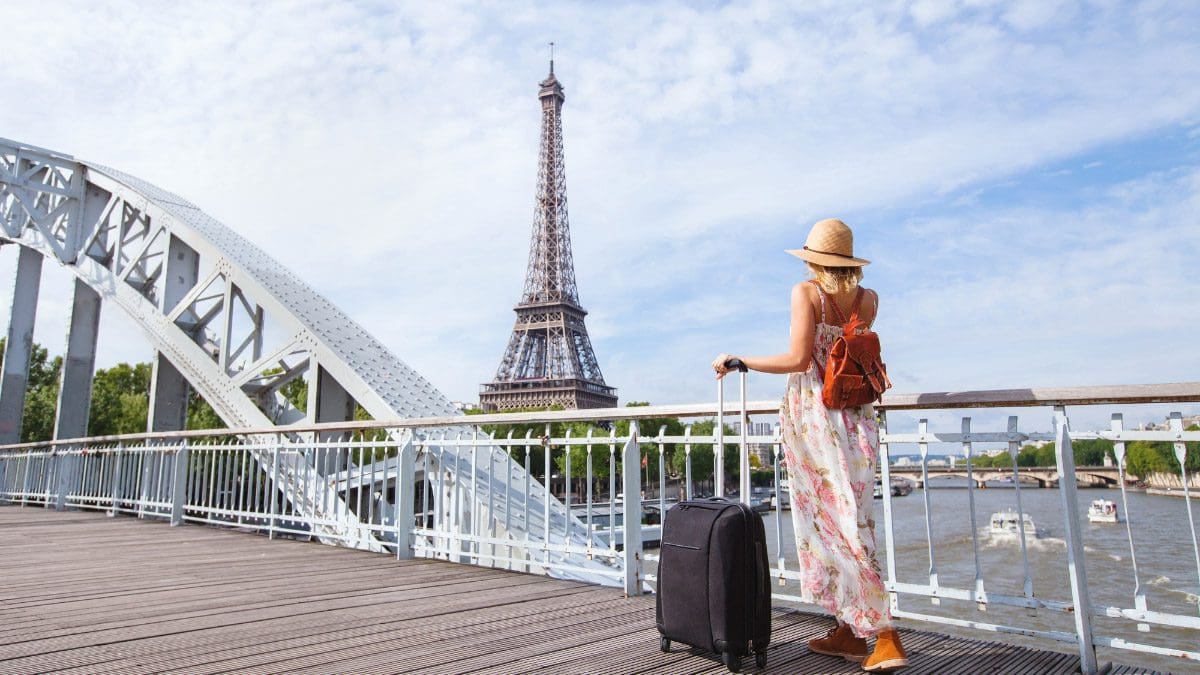 A woman holding onto a suitcase in front of the Eiffel Tower leveraging employee performance incentives.
