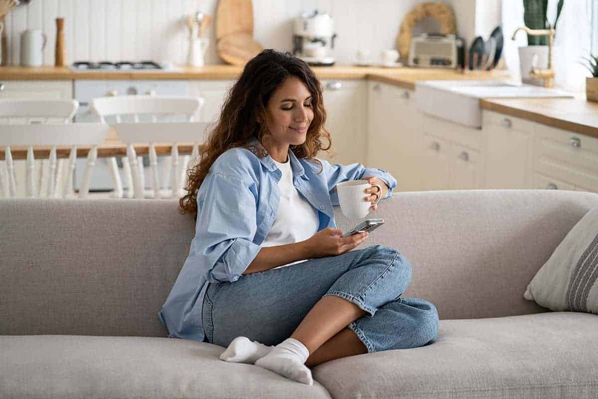 happy young woman using smartphone resting on couch using her loyalty rewards