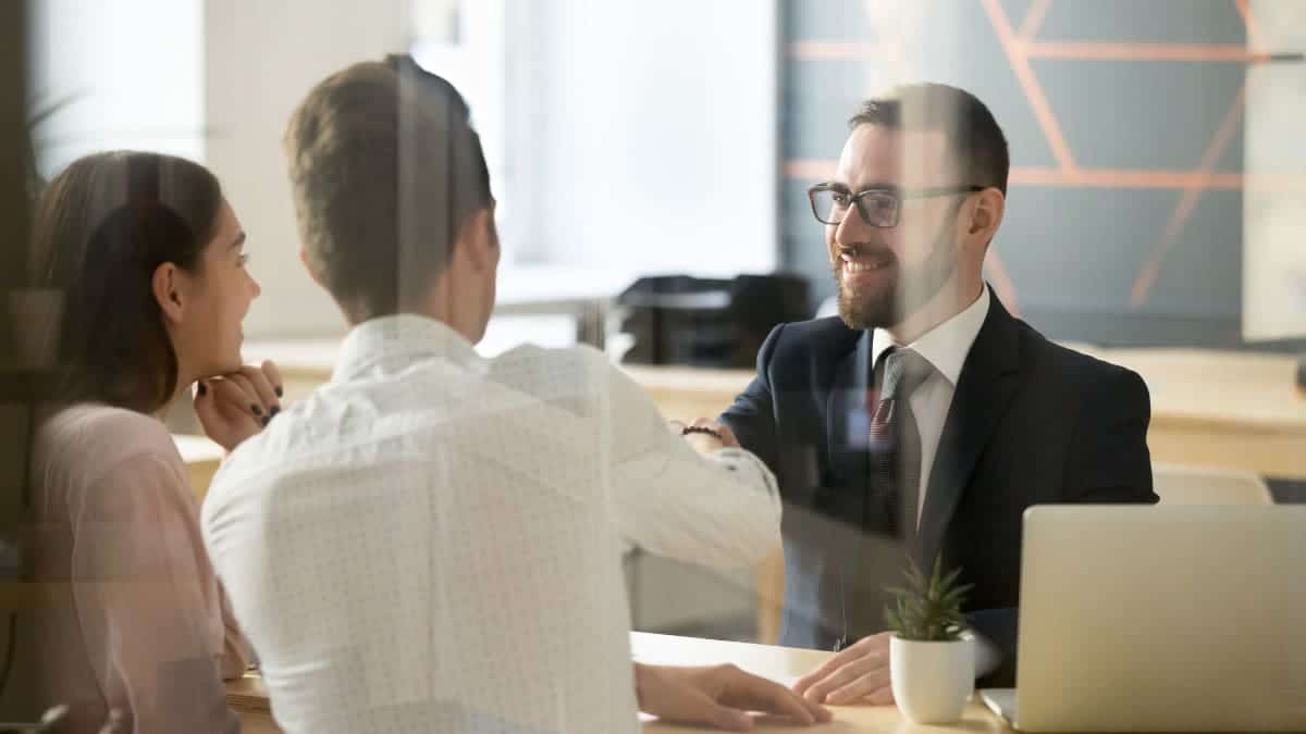 A couple is shaking hands in front of a bank employee.