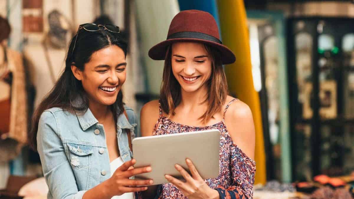 Two women laughing while looking at a tablet screen.