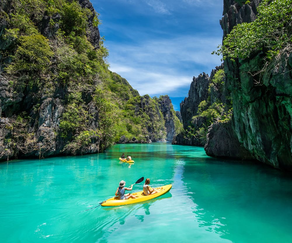 Tourists on kayaks exploring the natural sights around El Nido on a sunny day in Palawan Island, Philippines.