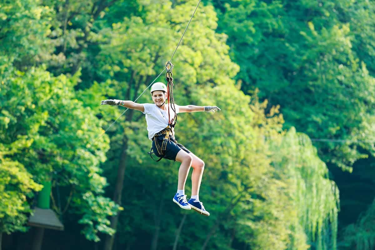 Happy child in white t-shirt and helmet having fun ziplining in experiential travel.