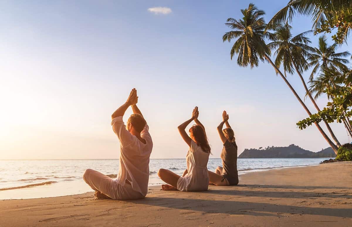 People practicing wellness meditation on a beach at sunrise during experiential travel.