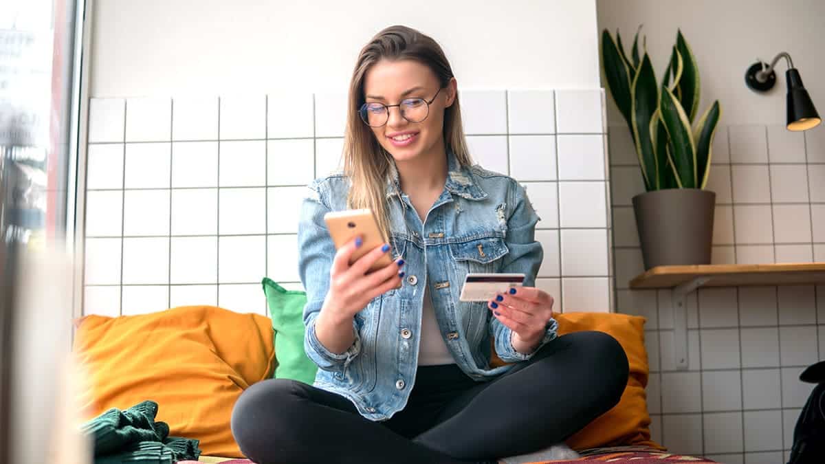 A young woman participating in a loyalty program using her loyalty card and smartphone to make purchases.