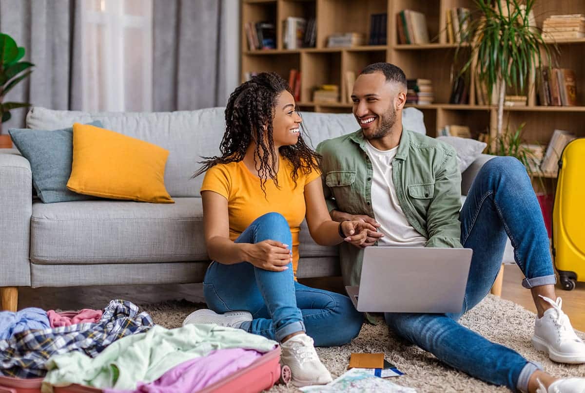 A couple sits on the floor, happily booking a trip to a vacation rental.