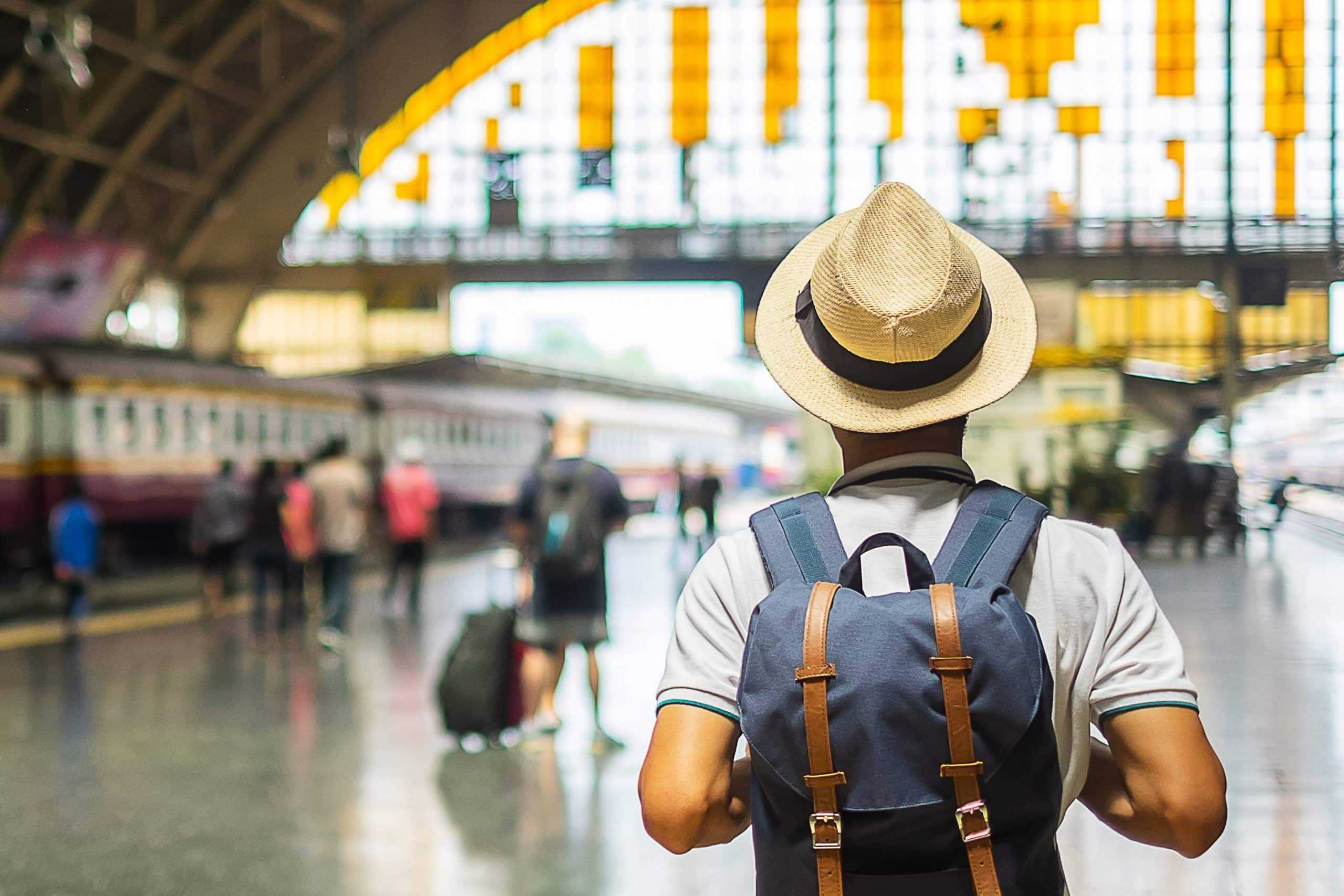 Traveler with backpack and hat walking through a train station 