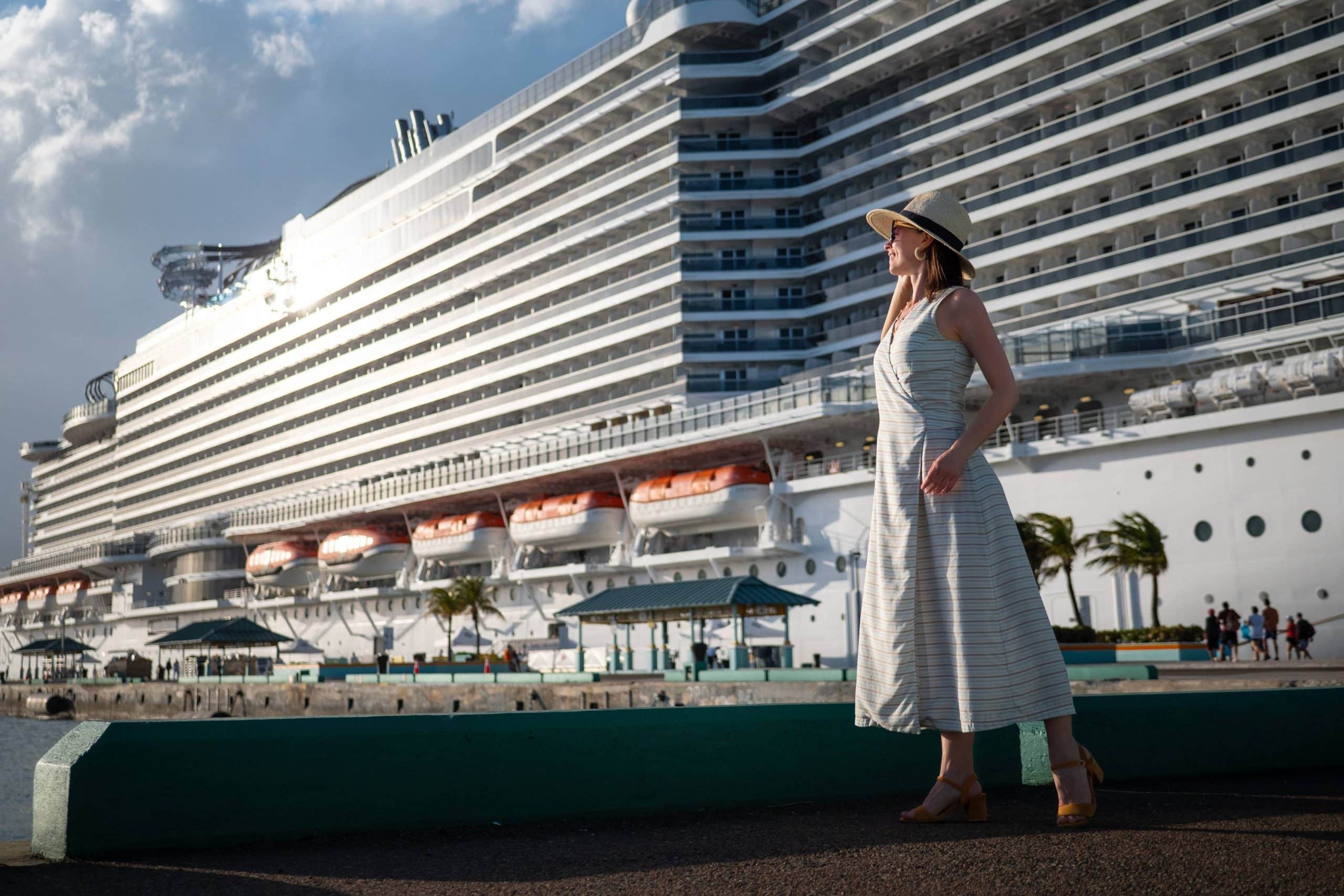 Traveler poses beside a docked cruise ship on a sunny day.