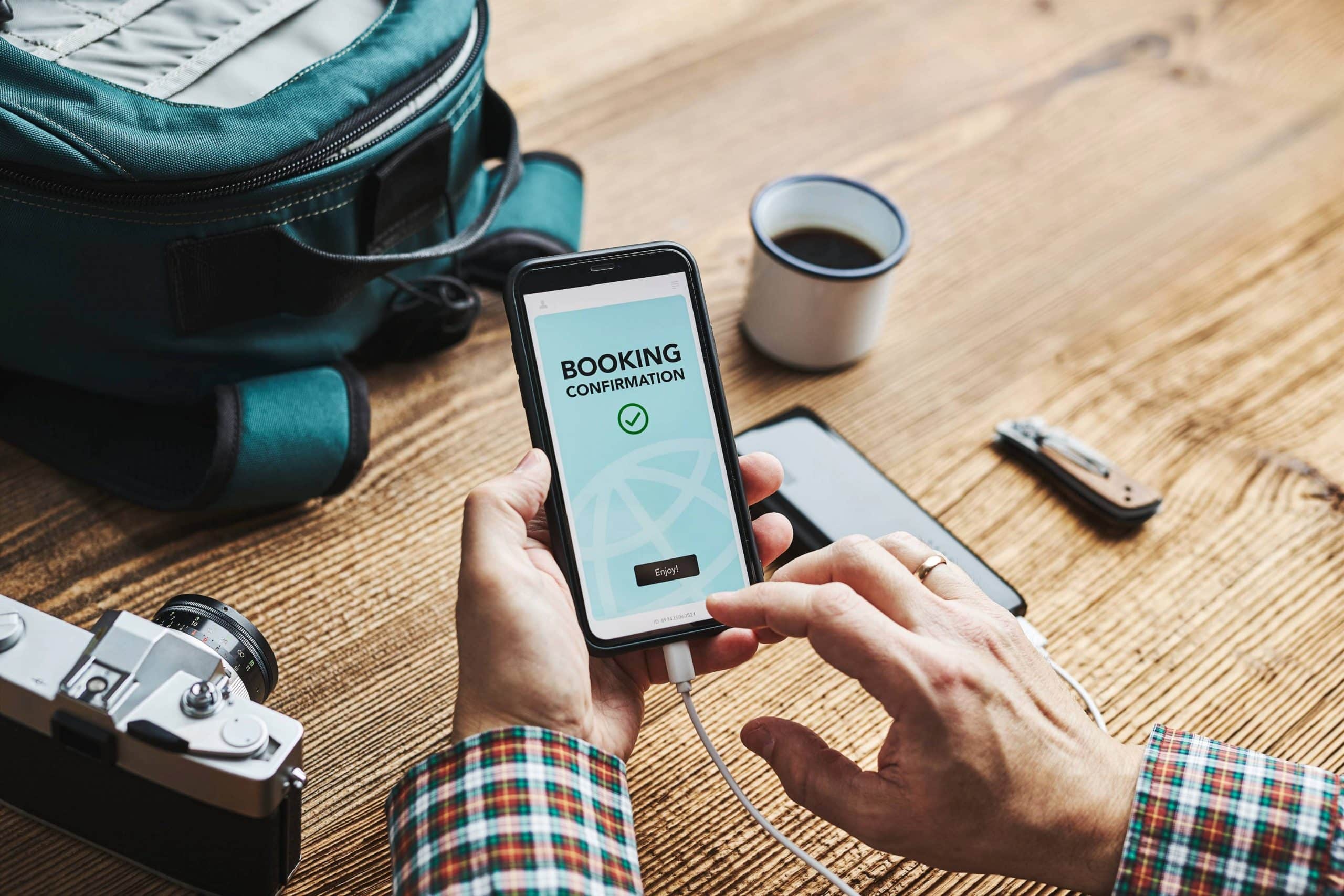 Person holding a smartphone showing a travel booking confirmation on a wooden desk
