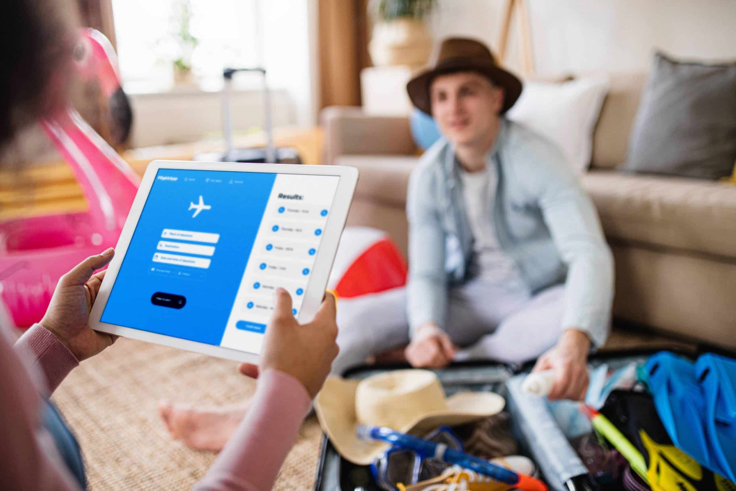Person using a tablet travel app to search and book flights while packing for a trip