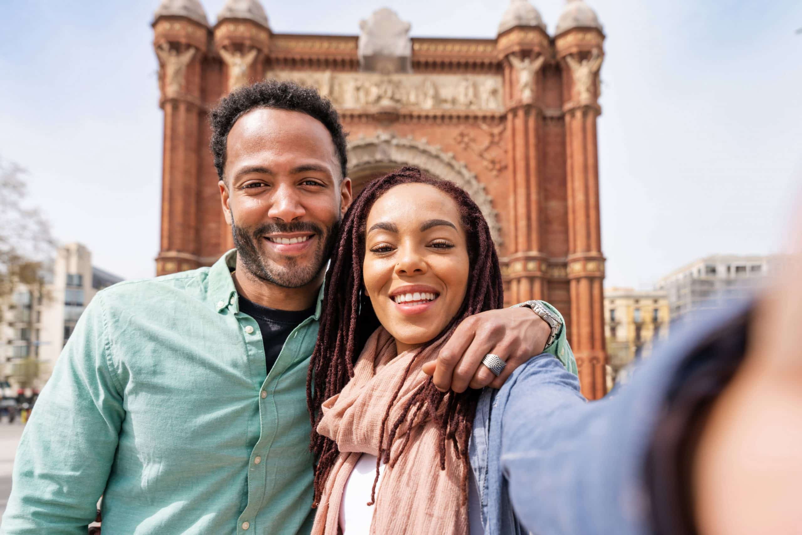 Smiling couple taking a selfie in front of a historic landmark while traveling together