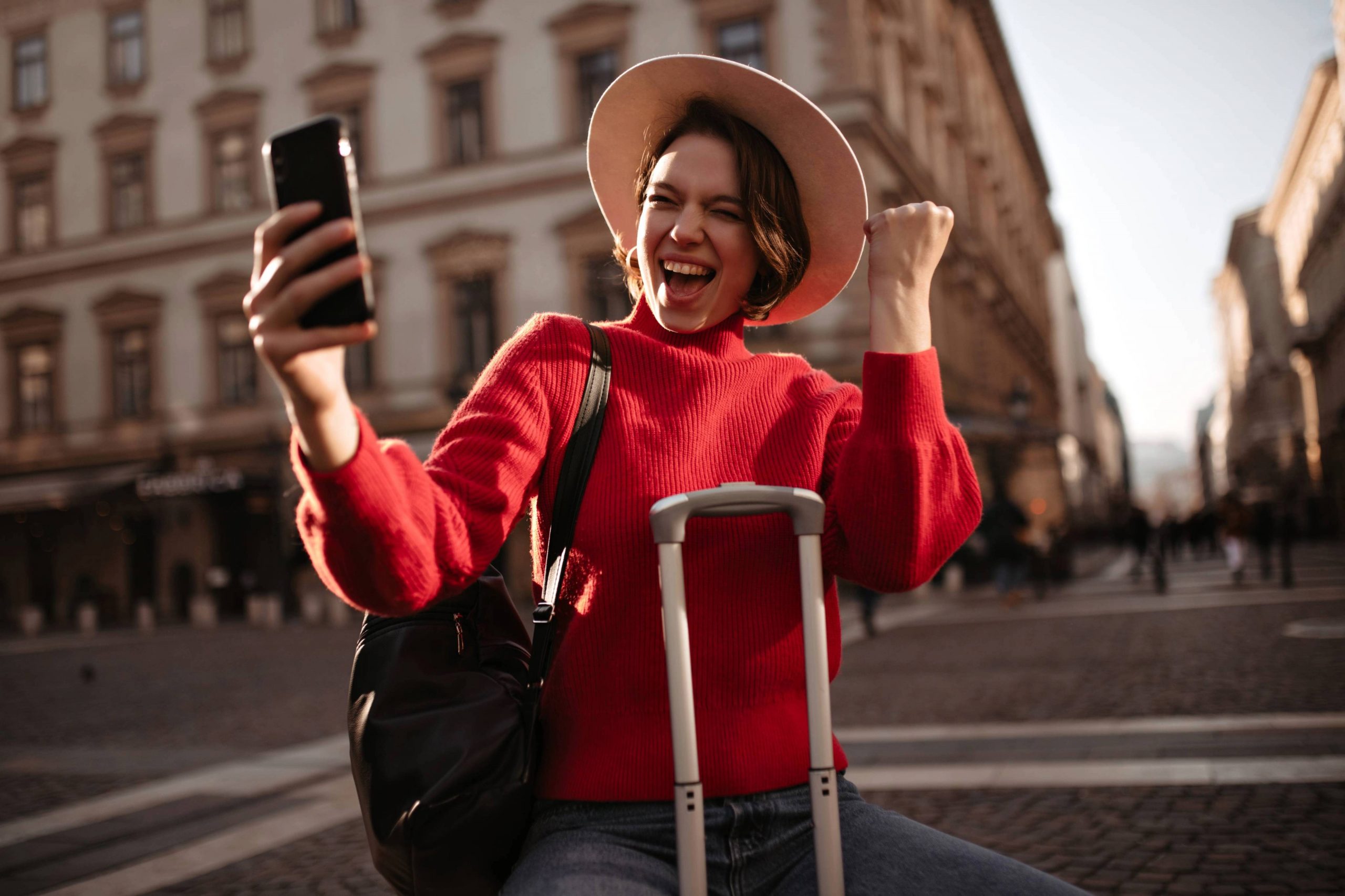 Traveler using a mobile travel app while standing with luggage in a city destination