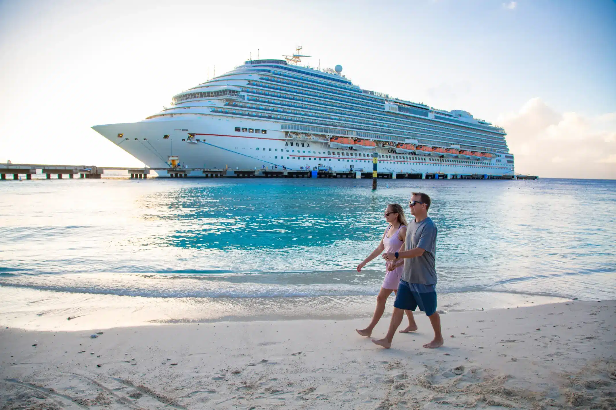 two people walk on the beach in front of a cruise ship